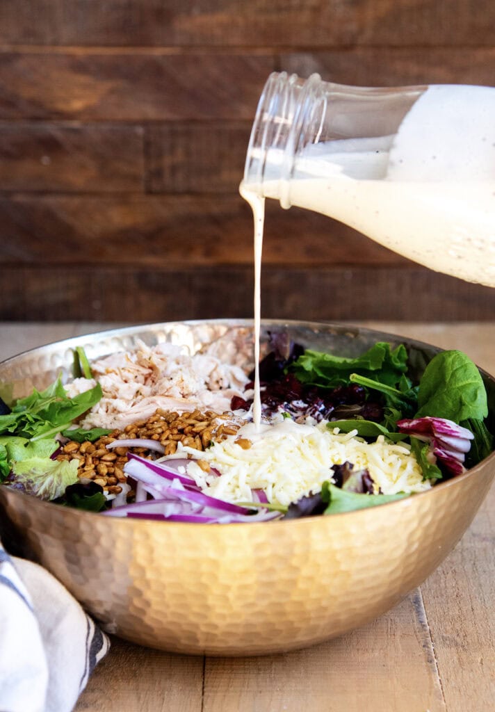 Poppy seed dressing being poured out of a bottle onto a salad.