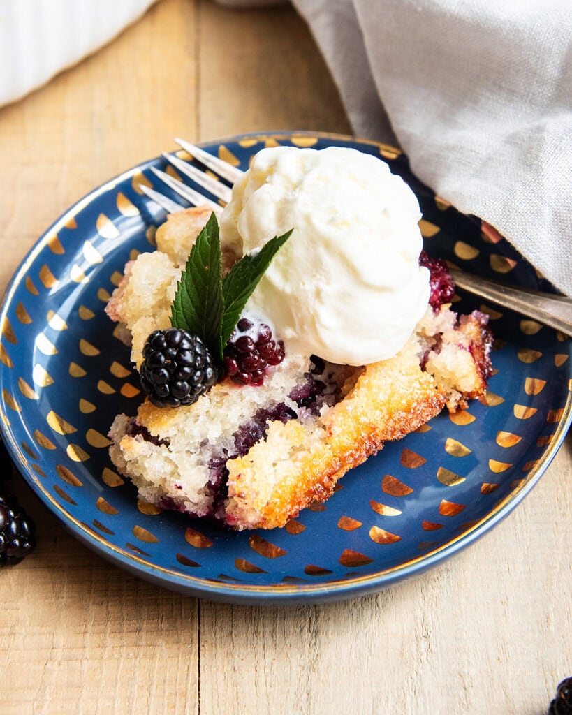 A scoop of blackberry cobbler on a plate topped with a scoop of vanilla ice cream.