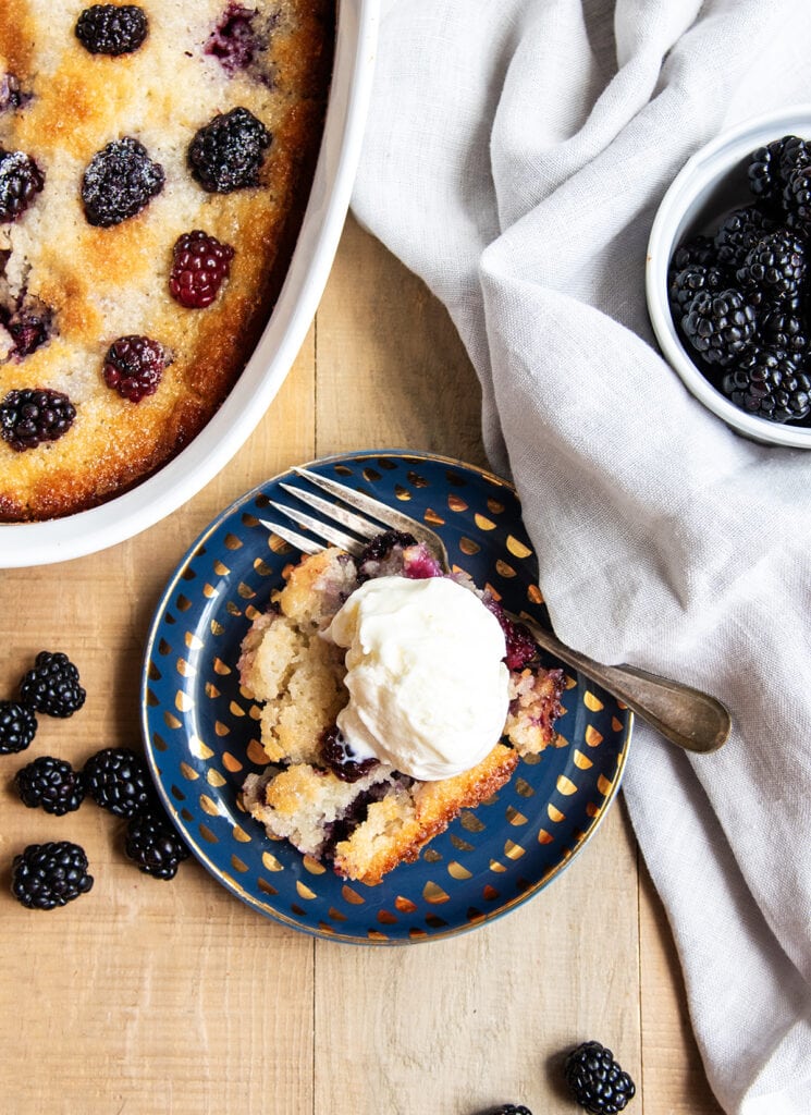 A scoop of blackberry cobbler on a plate topped with a scoop of vanilla ice cream.