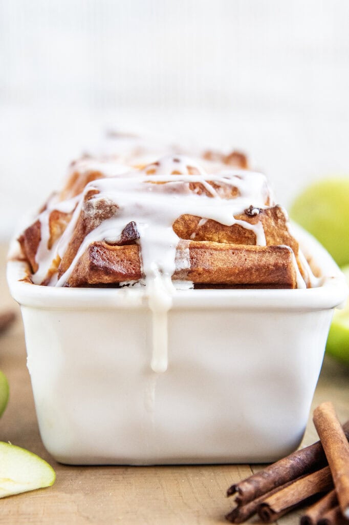 Apple Fritter Pull Apart bread topped with vanilla glaze in a white loaf pan.