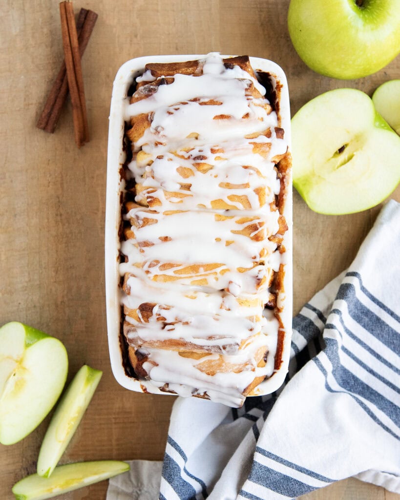 An above view of a loaf of apple fritter bread in a white bread pan, topped with a vanilla glaze.