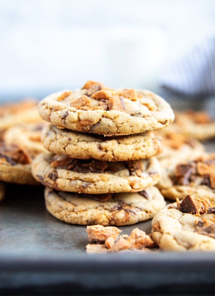 A stack of four peanut butter and butterfinger cookies on a cookie sheet.
