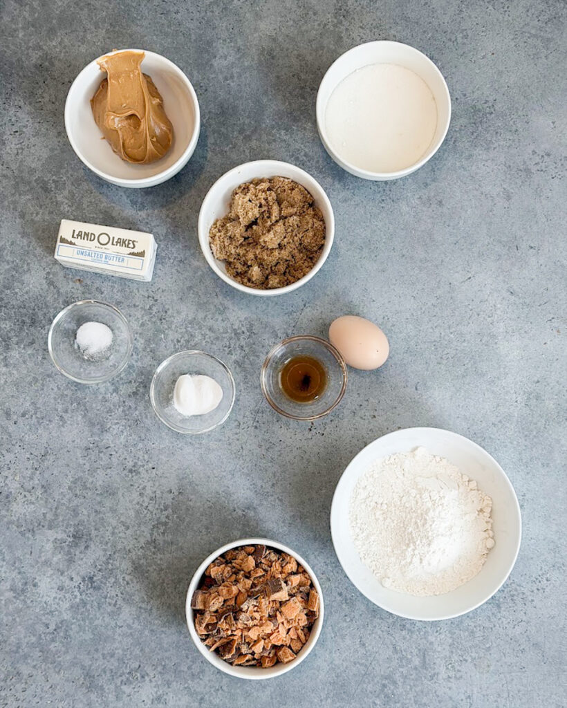 Small bowls of the ingredients needed to make peanut butter butterfinger cookies, like flour, butterfingers, sugar,egg, and butter.