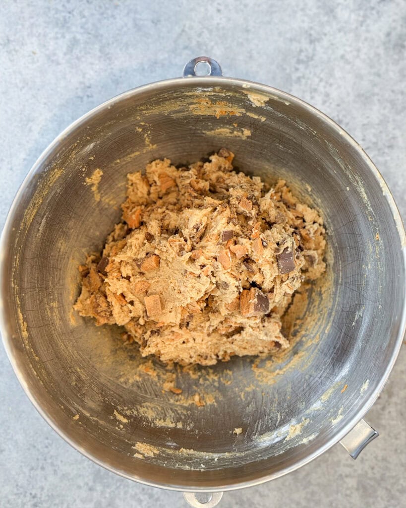 Peanut butter cookie dough full of butterfinger pieces in a large metal bowl.
