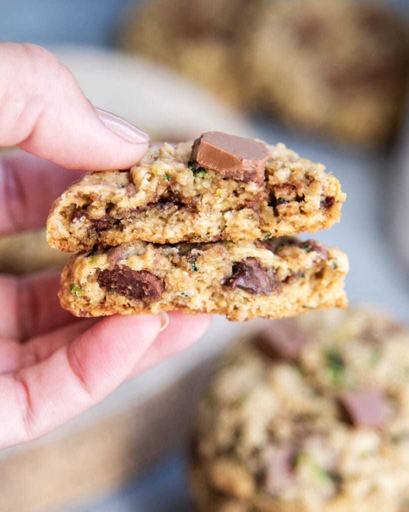 A hand holding two halves of a chocolate chip zucchini and oatmeal cookies