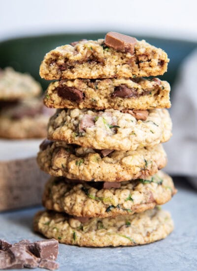 A stack of several chocolate chip zucchini cookies and the top cookies are broken in half showing the center of the cookies.