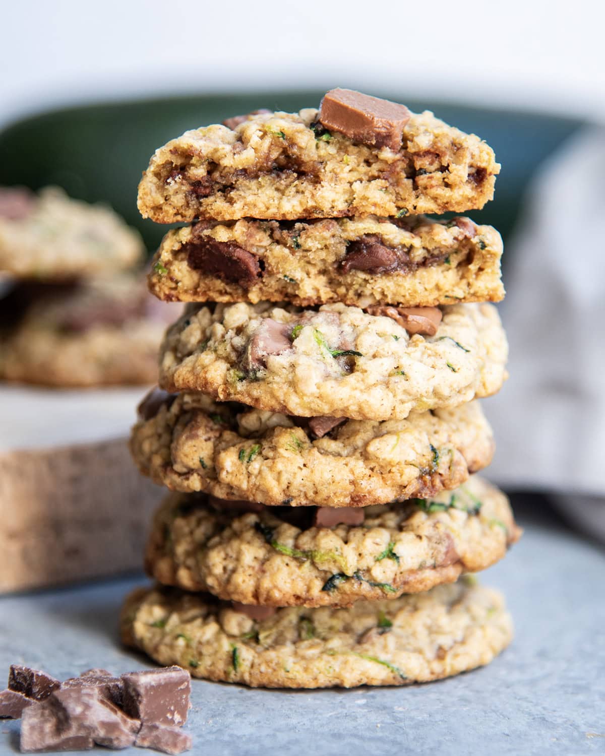 A stack of several chocolate chip zucchini cookies and the top cookies are broken in half showing the center of the cookies.