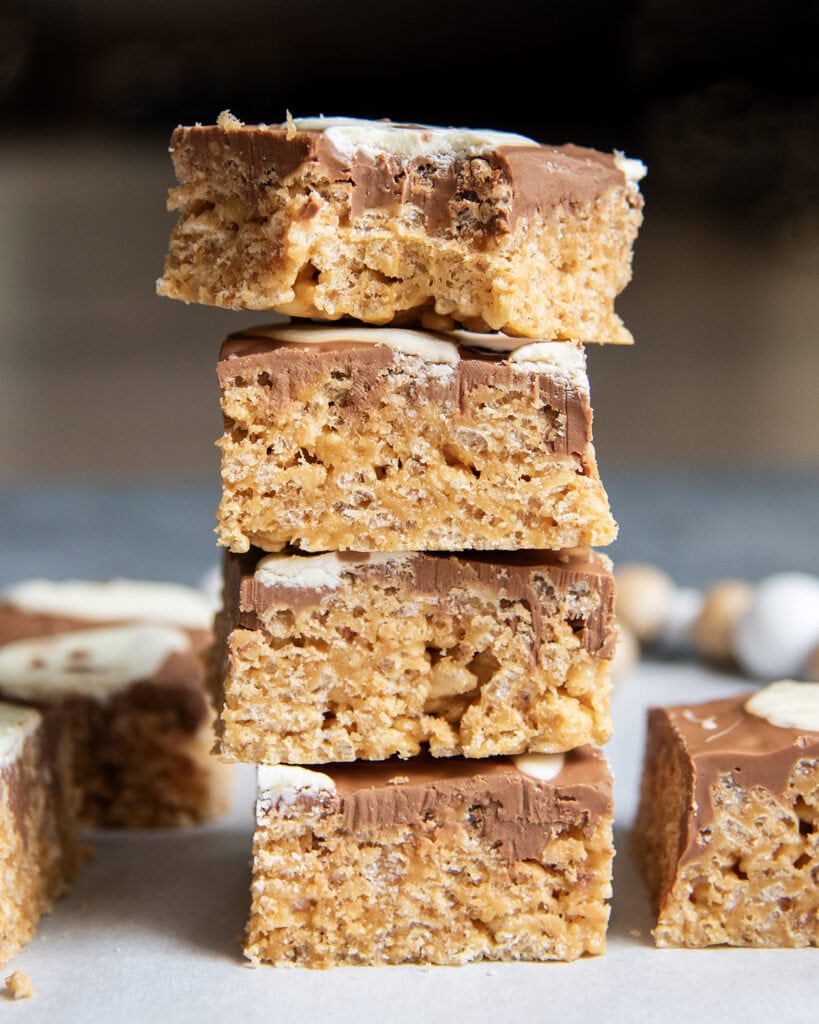 A stack of four scotcheroos topped with chocolate and white chocolate, and the top one has a bite out of it.