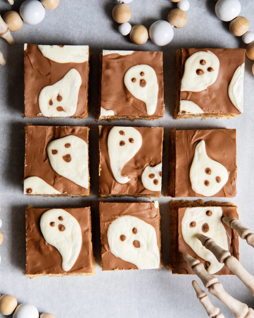 An above view of chocolate covered rice krispie treats with white chocolate ghosts on them.