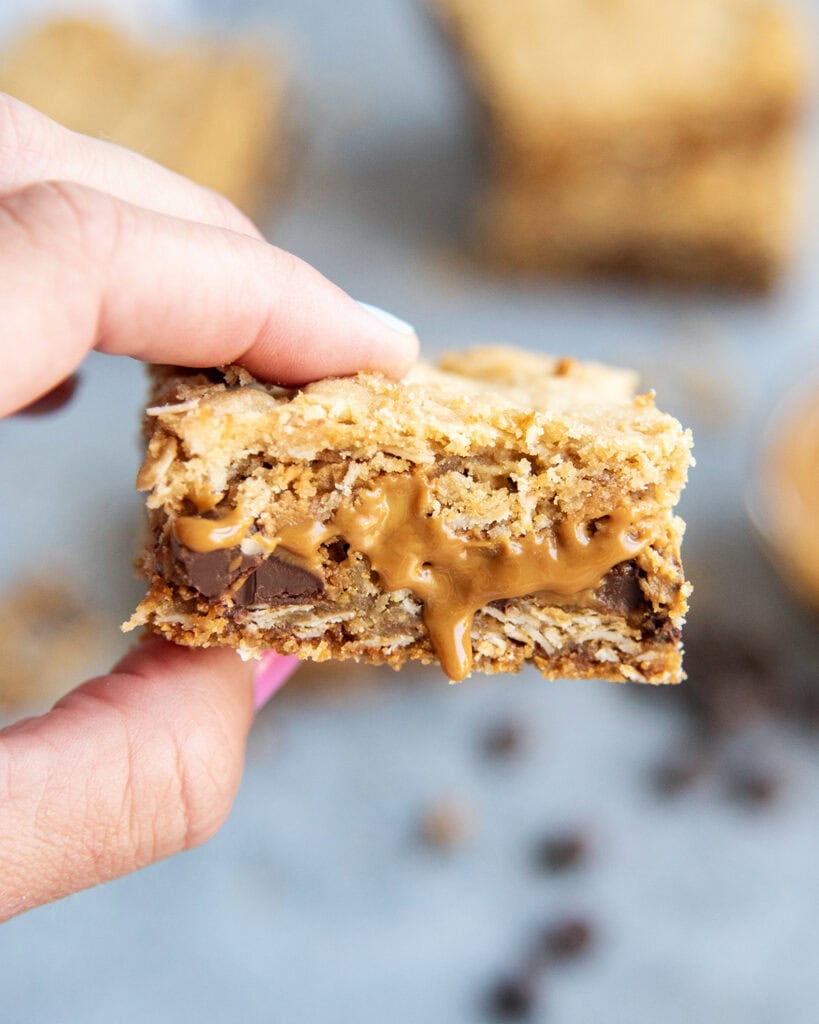 A hand holding a cookie butter oatmeal cookie bar with chocolate chips and cookie butter in the middle of oatmeal!
