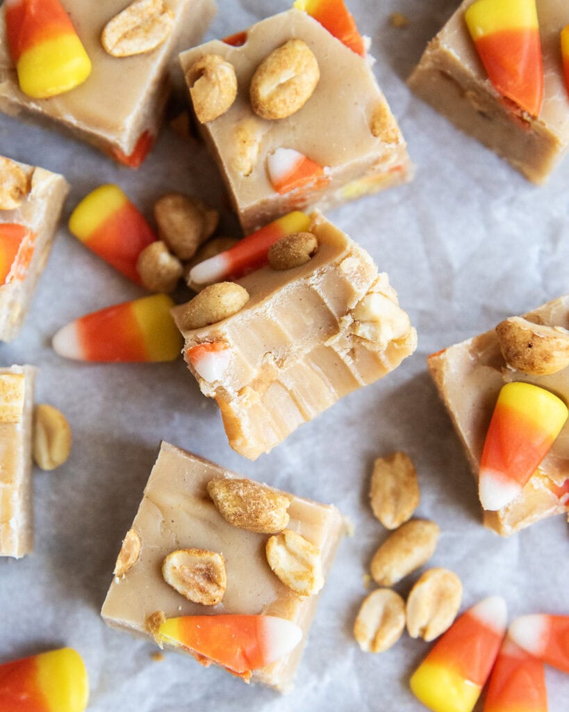 Pieces of peanut butter fudge with peanuts and candy corn pieces, and one piece of fudge has a bite out of it.
